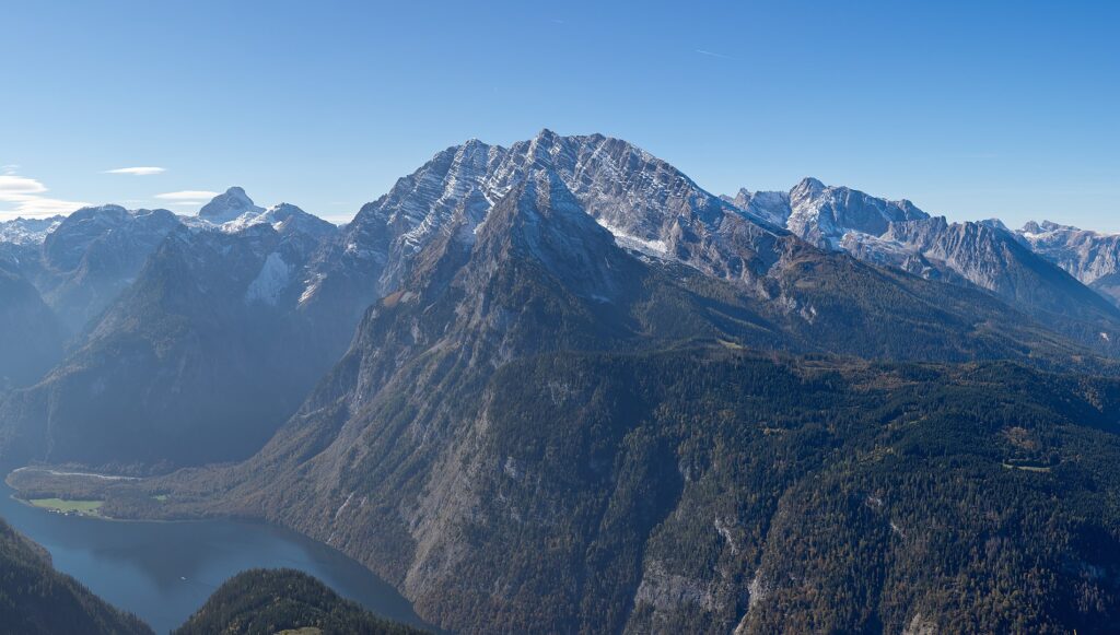 View of the Watzmann mountain from Jenner mountain in the Bavarian Alps, overlooking the Königssee. A mountainscape with a river valley under a clear blue sky.