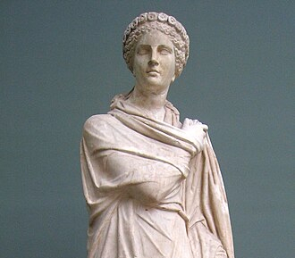 Detail of marble statue of Polyhymnia from Monte Calvo, Italy, 2nd century CE. A crowned figure with a solemn face and long, flowing robes either stands or dances. Her right arm is crossed over her chest, the hand touching her left shoulder. The left hand gathers up the robe beside her.